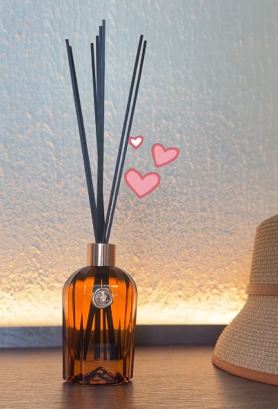 A stylish reed diffuser with black reeds in an amber glass bottle, displayed on a wooden surface.