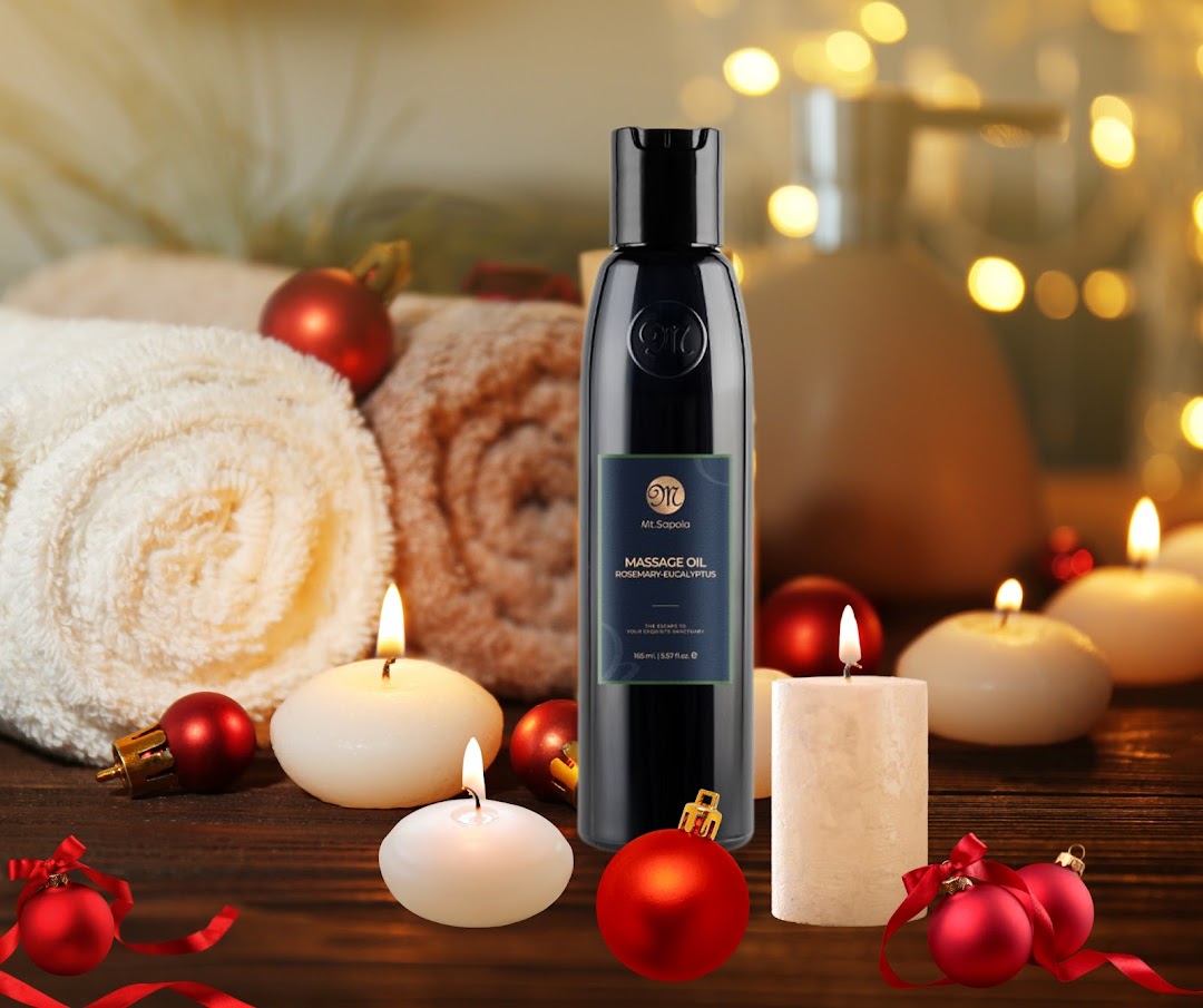 A Mt.Sapola massage oil bottle surrounded by candles, towels, and festive ornaments on a wooden surface.