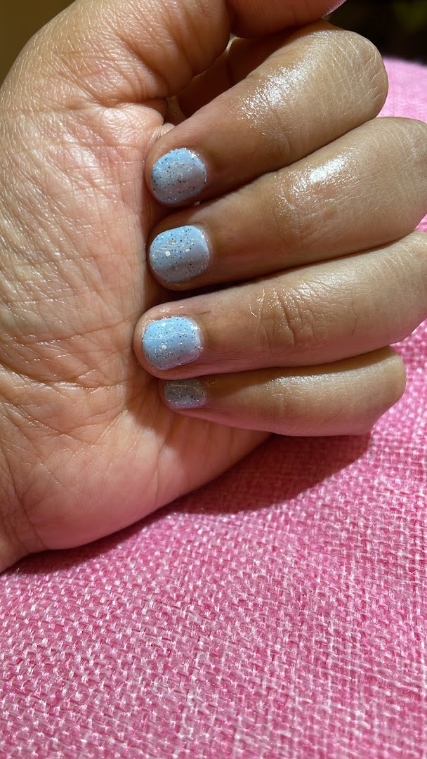 A hand showcasing light blue glitter nail polish on a pink textured surface.