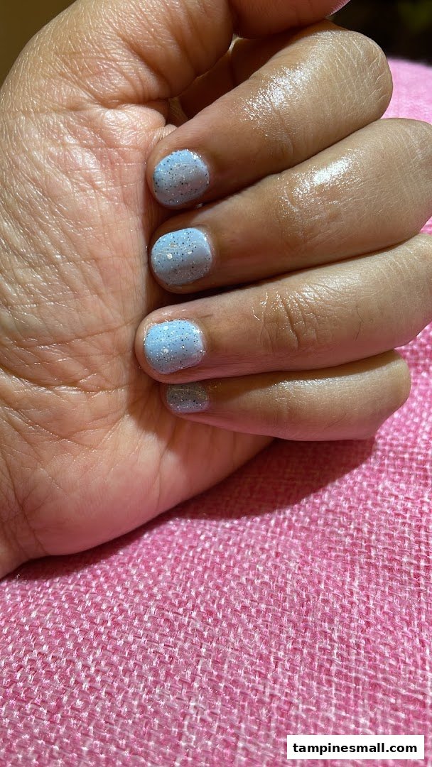 A hand showcasing light blue glitter nail polish on a pink textured surface.