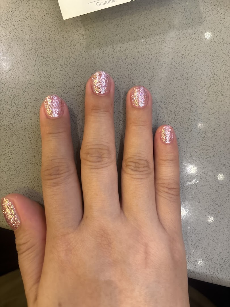 A hand showcasing freshly applied pink glitter nail polish on a grey countertop.