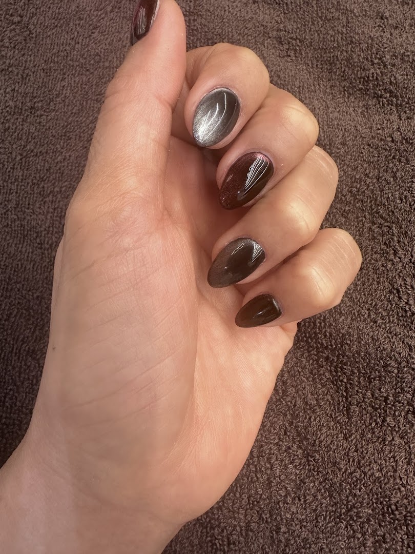 A hand showcasing freshly manicured nails with dark and metallic cat-eye polish.