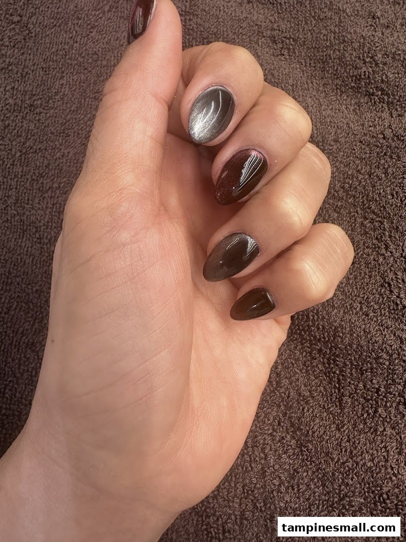 A hand showcasing freshly manicured nails with dark and metallic cat-eye polish.