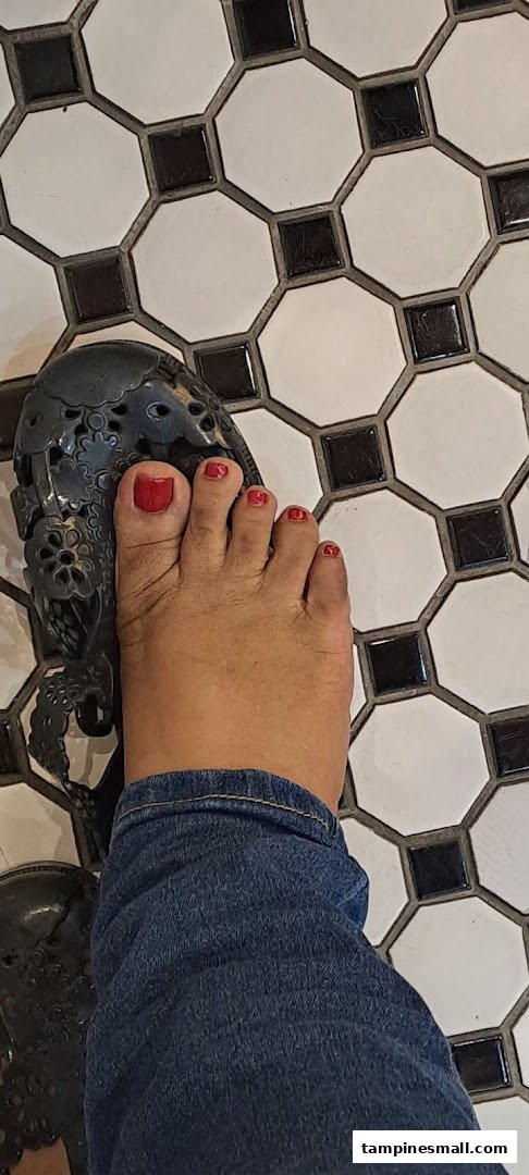 A close-up of a foot with vibrant red painted toenails and a decorative sandal on a black and white tiled floor.