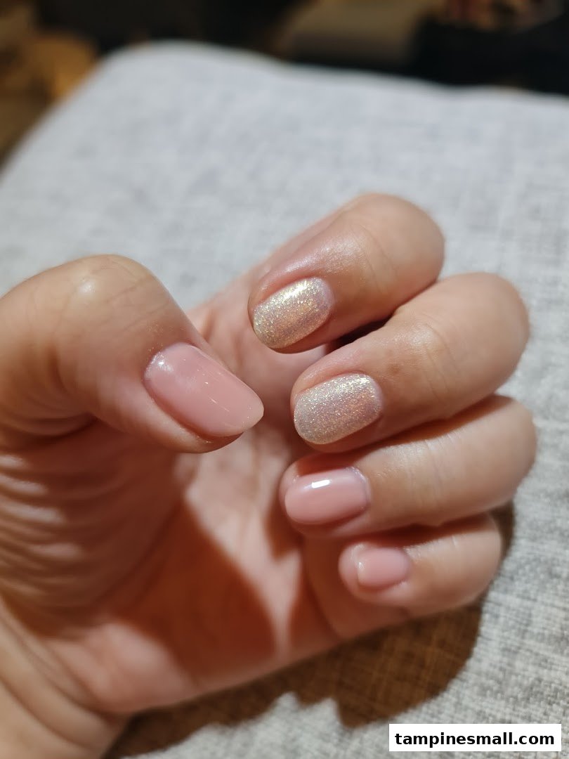 A hand showcasing a fresh manicure with a mix of nude and glitter nail polish.