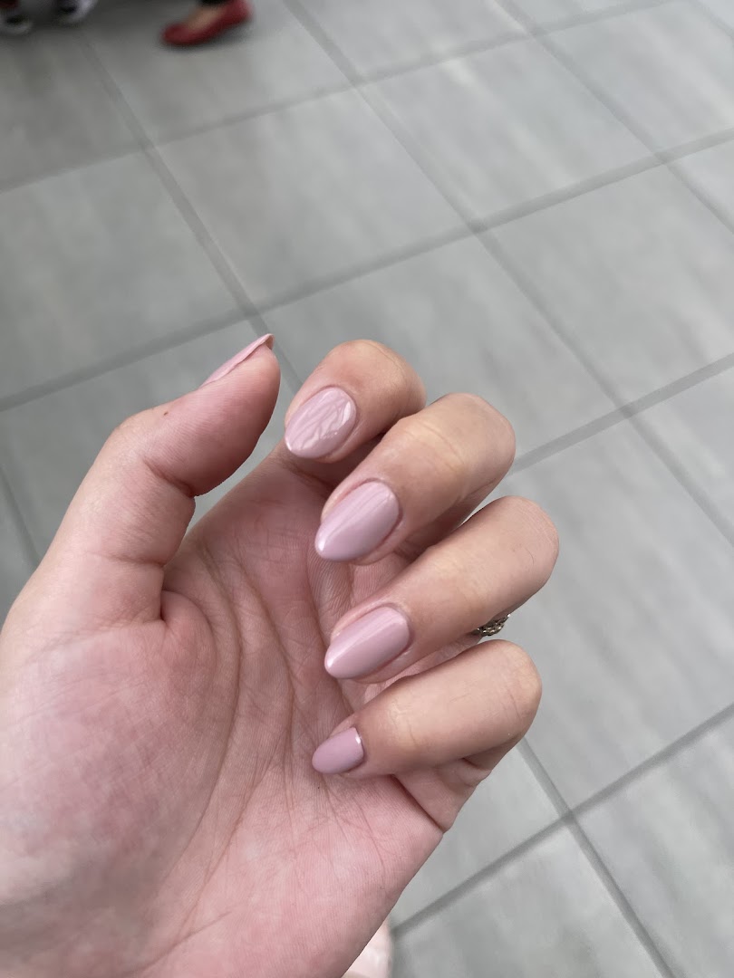 A hand showcasing freshly manicured nails with light pink polish, highlighting the salon's service quality.