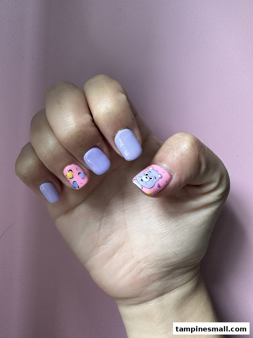 A hand showcasing vibrant purple and pink nails with playful cartoon and heart designs.