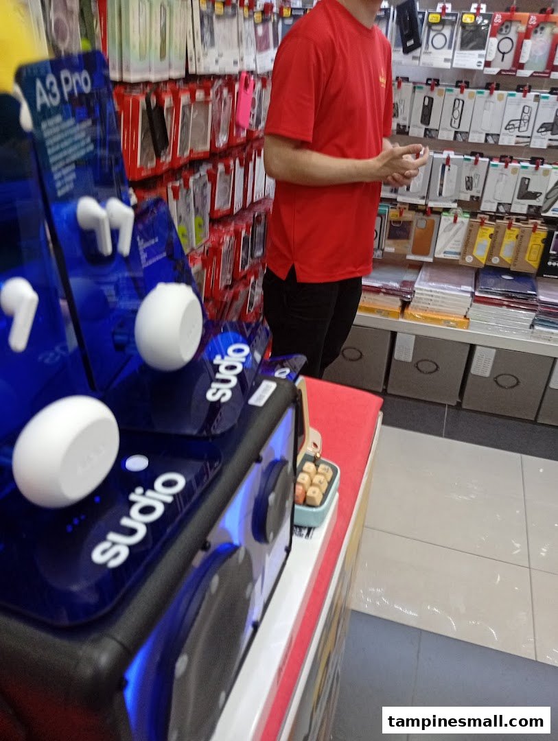 A person in a red shirt stands near a display of Sudio earbuds and various phone accessories in a tech shop.