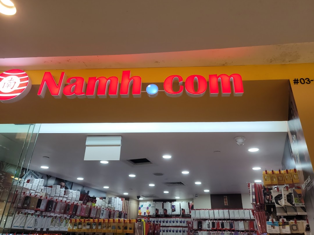 The illuminated storefront of Namh.com, a tech accessories shop, showcasing its entrance and interior products.
