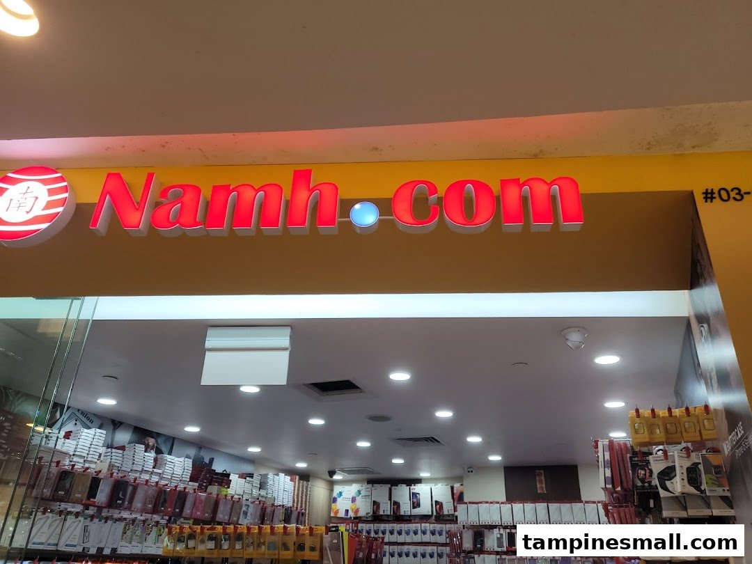 The illuminated storefront of Namh.com, a tech accessories shop, showcasing its entrance and interior products.
