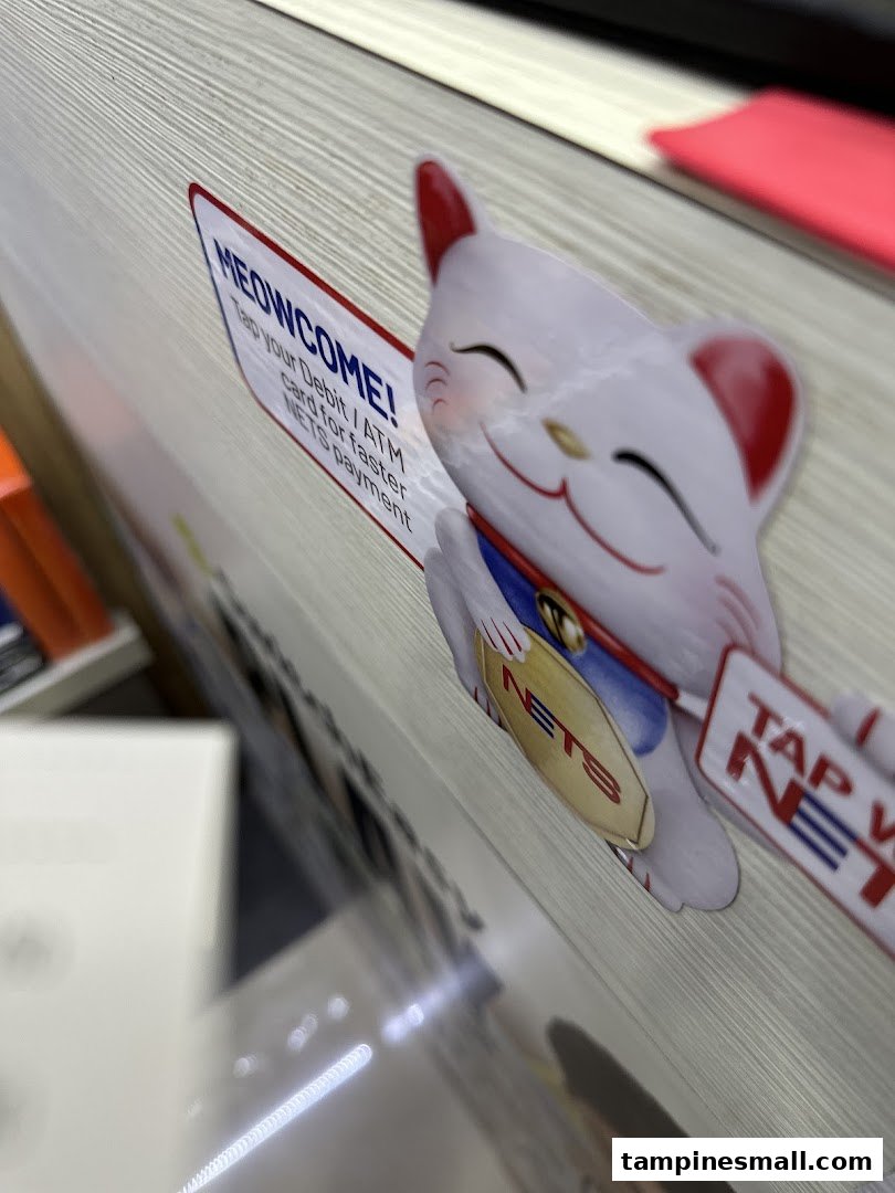 A close-up of a Maneki-neko sticker promoting NETS payment with the text "MEOWCOME!".