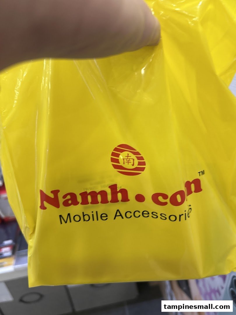 A person holds a bright yellow shopping bag featuring the 'Namh.com Mobile Accessories' logo.