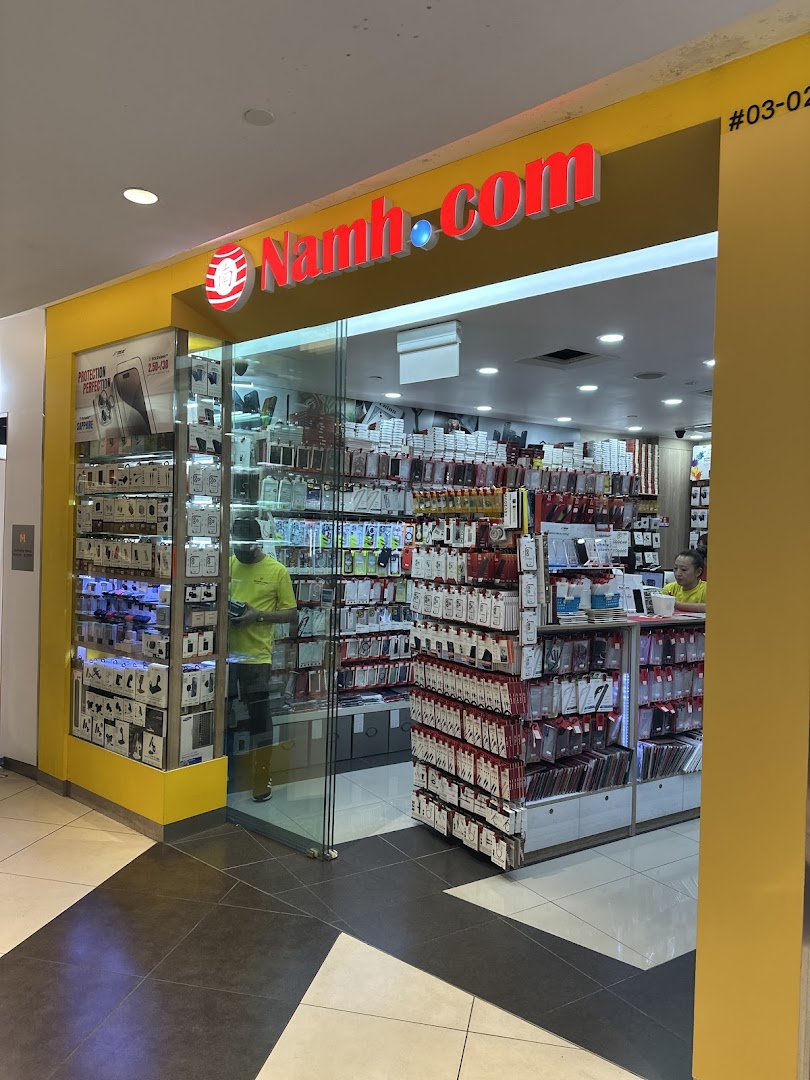 The shop front of Namh.com, an electronics and phone accessories store, with displays of products and staff inside.