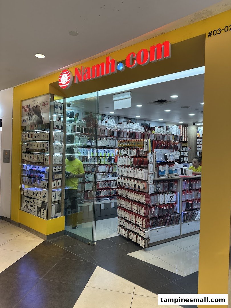 The shop front of Namh.com, an electronics and phone accessories store, with displays of products and staff inside.
