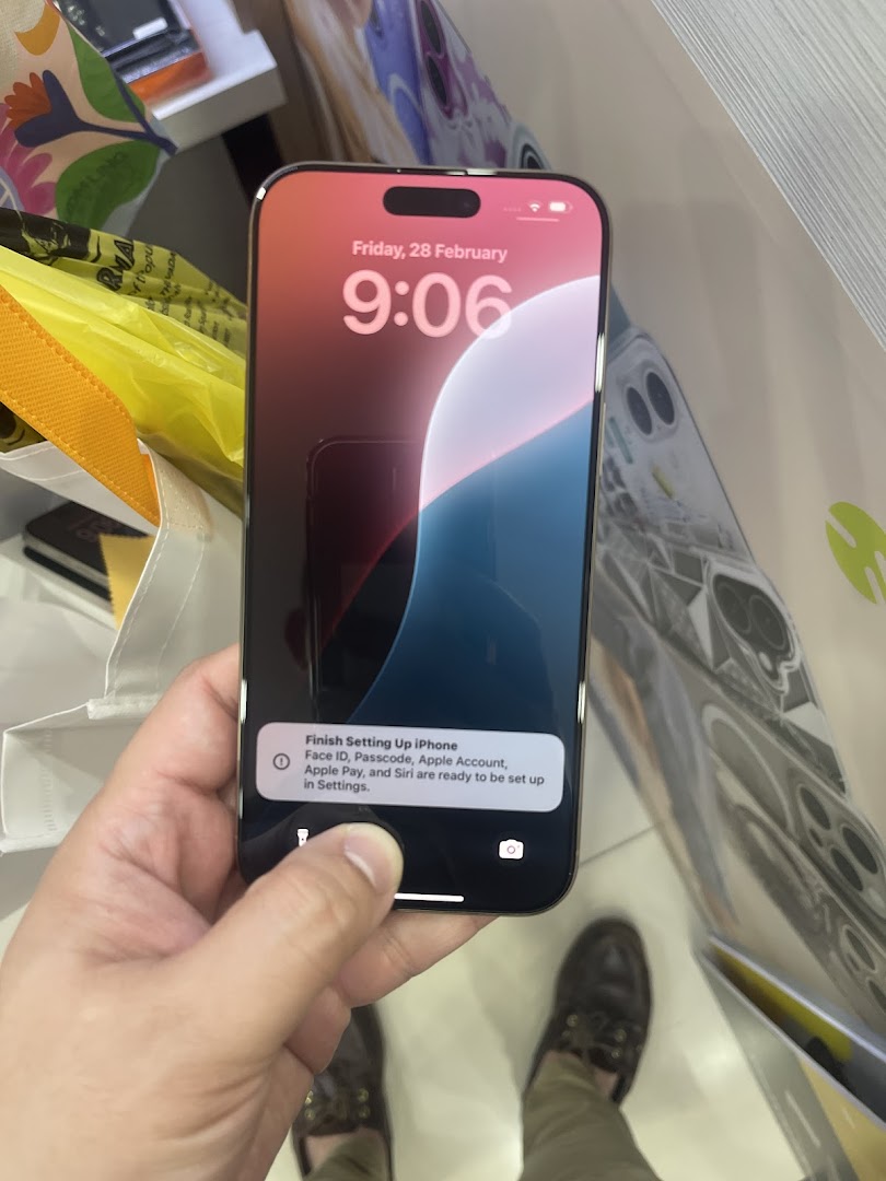 A person holds a new iPhone displaying the setup screen, with shopping bags visible in a retail environment.