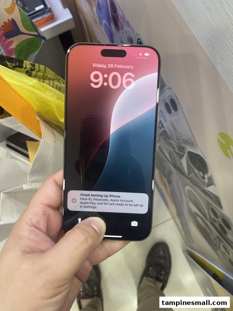 A person holds a new iPhone displaying the setup screen, with shopping bags visible in a retail environment.