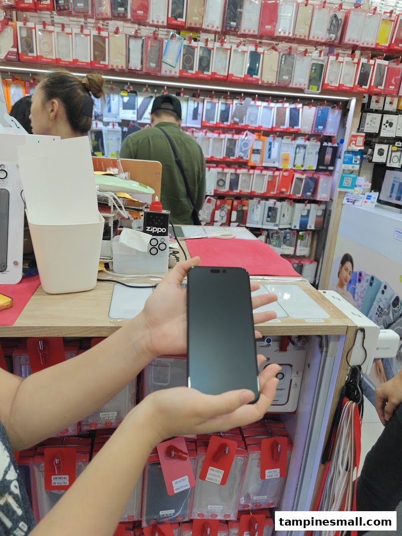 A customer holds a smartphone in a tech accessories shop, surrounded by numerous phone cases and other gadgets.