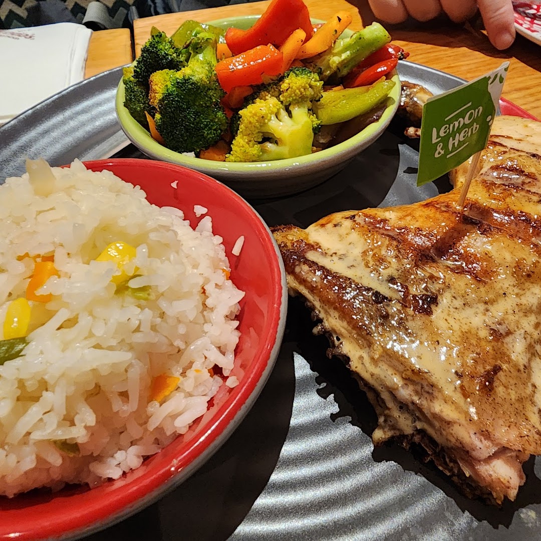 A plate of Nando's flame-grilled PERi-PERi chicken with rice and roasted vegetables, featuring a 'Lemon & Herb' flag.