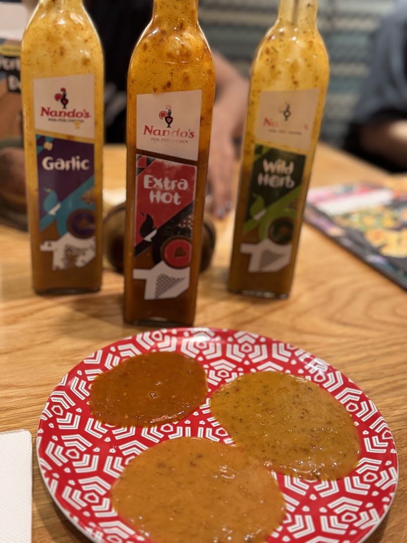 Three Nando's PERi-PERi sauce bottles (Garlic, Extra Hot, Wild Herb) and a plate with sauce samples.