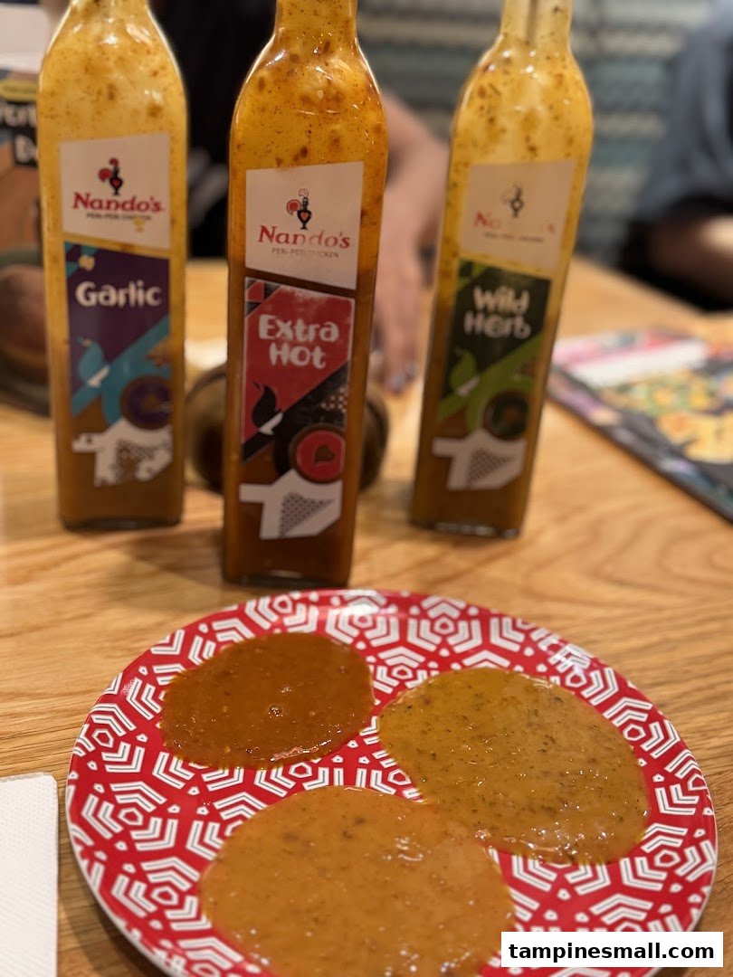 Three Nando's PERi-PERi sauce bottles (Garlic, Extra Hot, Wild Herb) and a plate with sauce samples.