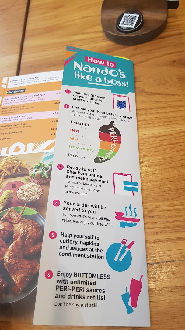 A Nando's table setting showing a menu, ordering guide, and a glimpse of flame-grilled PERi-PERi chicken.