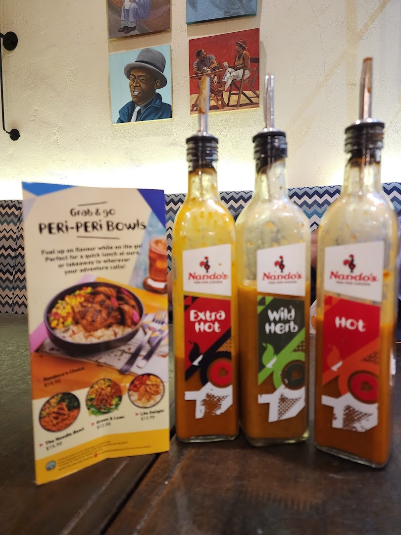 Three Nando's PERi-PERi sauce bottles and a promotional standee for PERi-PERi Bowls on a table.