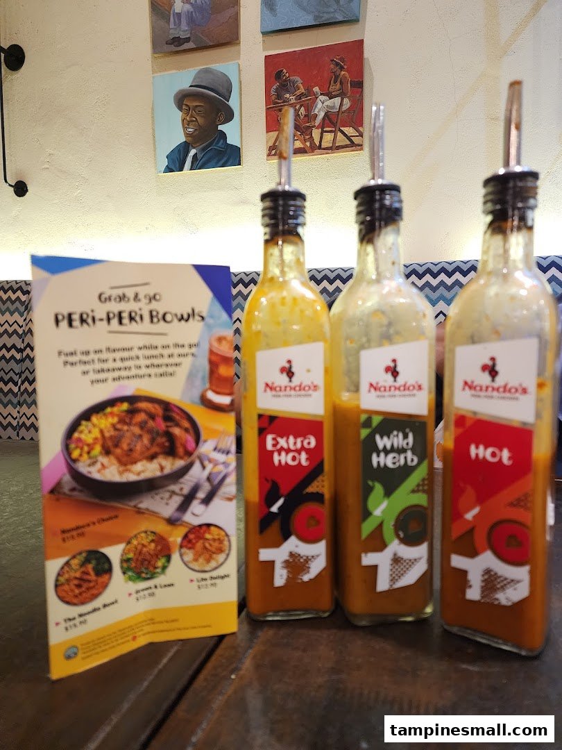 Three Nando's PERi-PERi sauce bottles and a promotional standee for PERi-PERi Bowls on a table.
