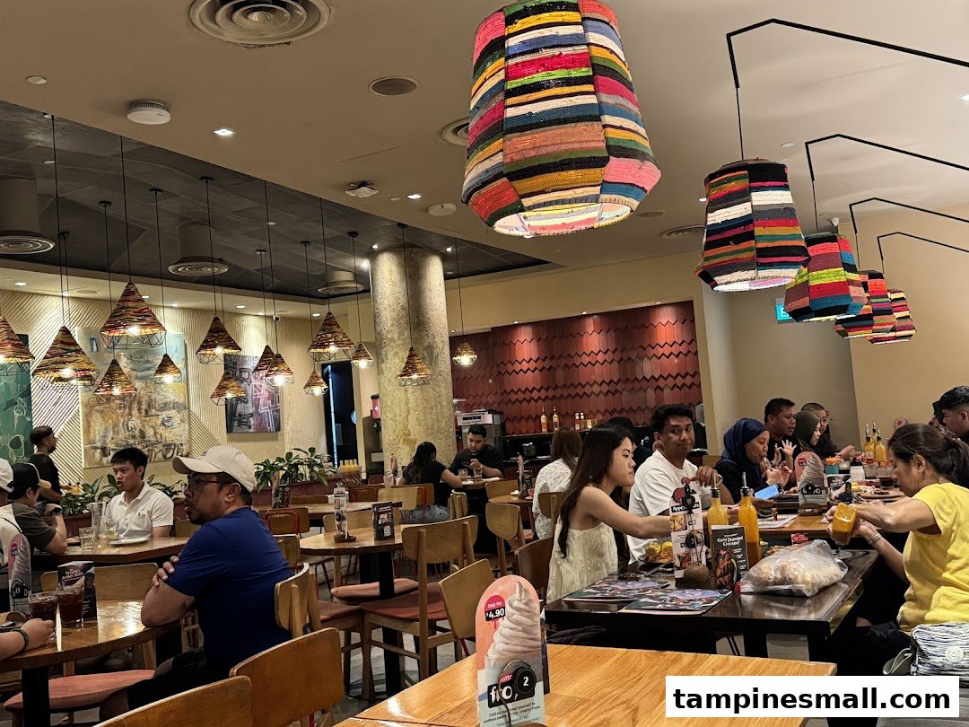Diners enjoy meals in the vibrant, well-lit interior of Nandos, featuring unique colorful and woven light fixtures.