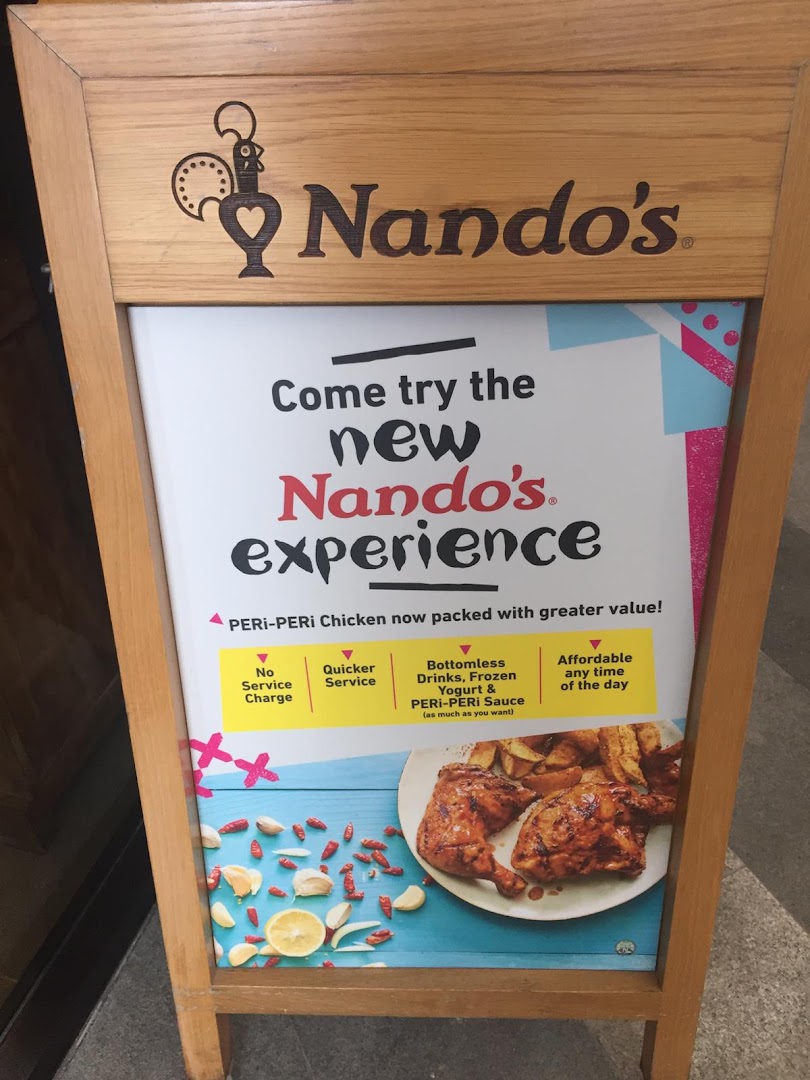 An A-frame sign outside Nando's advertises their new PERi-PERi chicken experience with value-added benefits.