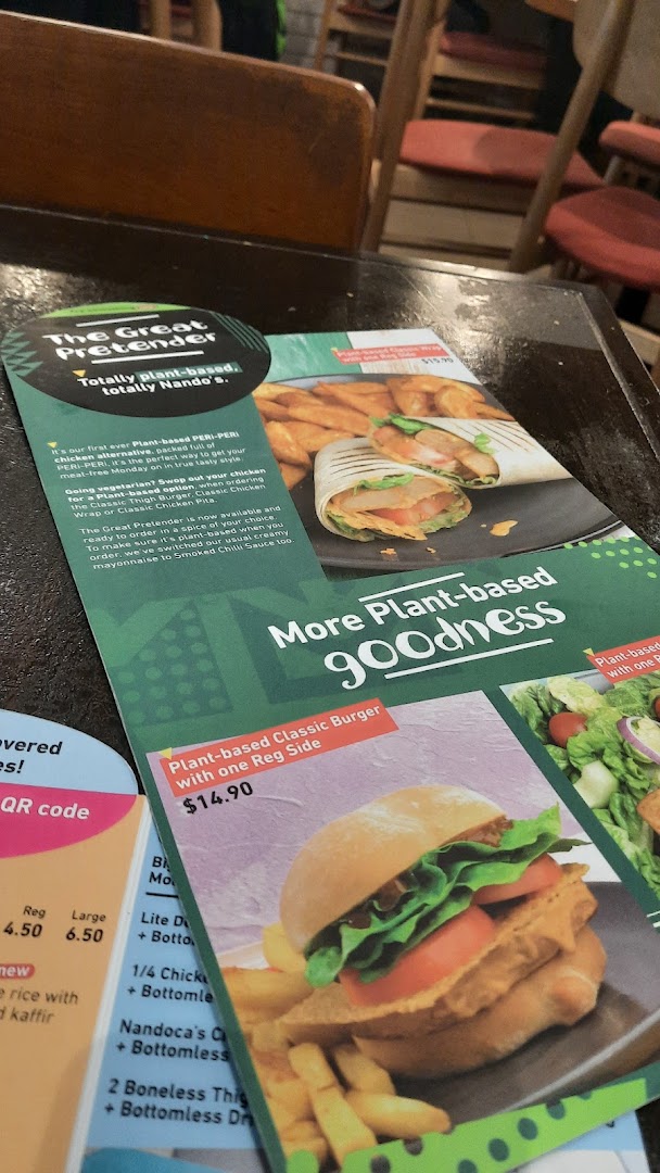 A Nando's menu flyer on a table, highlighting new plant-based options and prices.