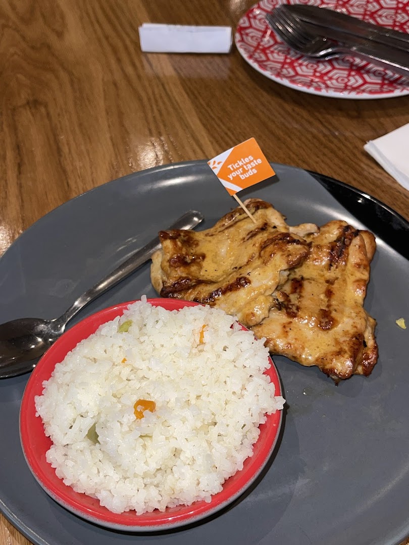A plate of flame-grilled chicken with rice, featuring a 'Tickles your taste buds' flag, served on a grey plate.