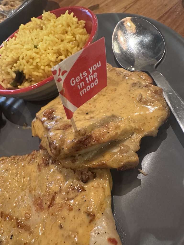A close-up of Nando's flame-grilled PERi-PERi chicken with creamy sauce, served with yellow rice and a branded flag.