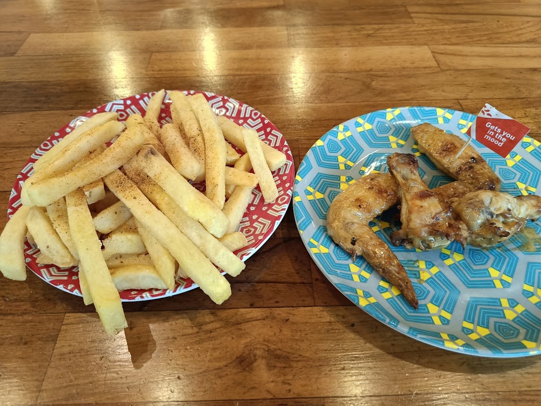 A plate of seasoned fries and a plate of flame-grilled chicken wings on a wooden table.