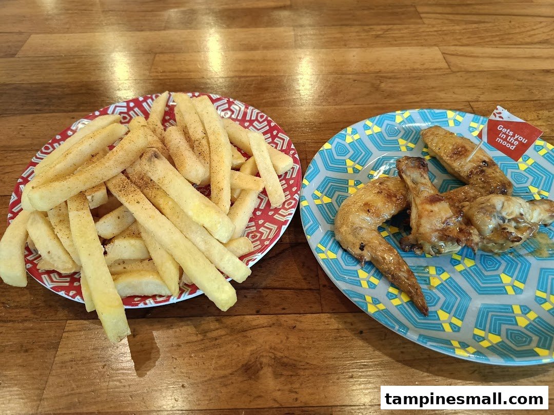A plate of seasoned fries and a plate of flame-grilled chicken wings on a wooden table.