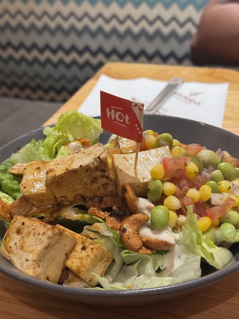 A vibrant salad bowl featuring tofu, corn, edamame, and cashews, with a 'Hot' flag.