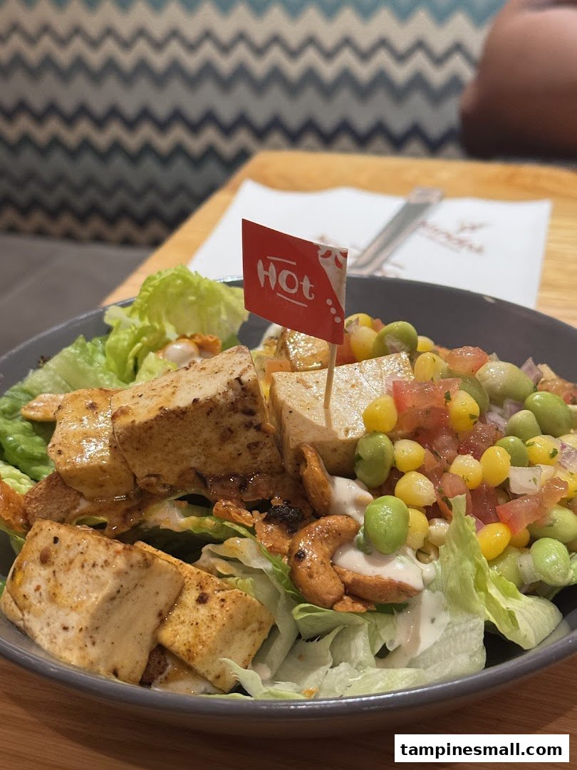 A vibrant salad bowl featuring tofu, corn, edamame, and cashews, with a 'Hot' flag.