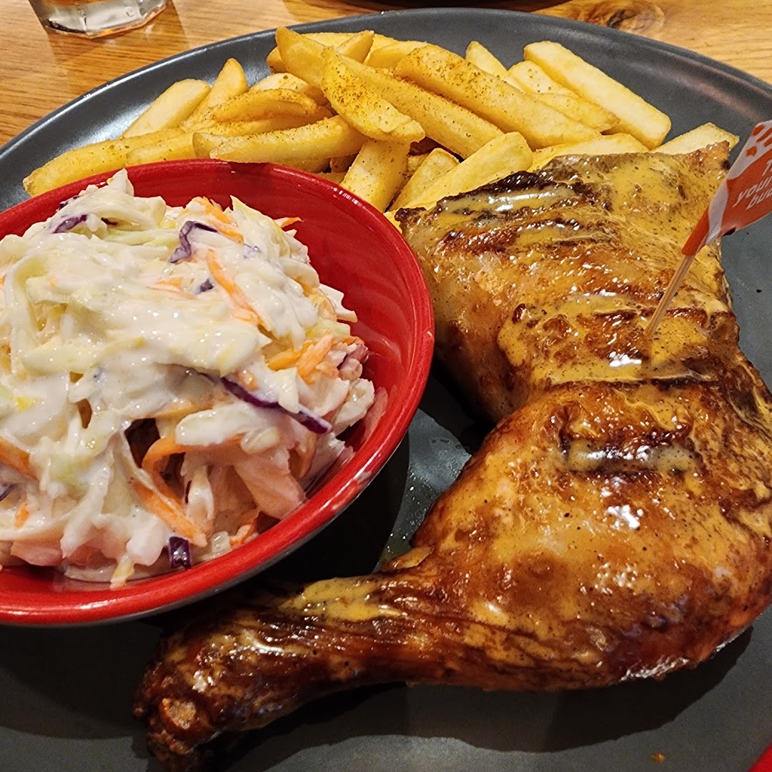 A plate of Nando's flame-grilled PERi-PERi chicken with fries and creamy coleslaw.