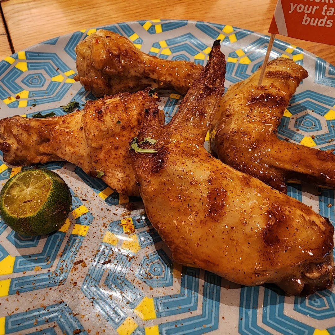 Close-up of flame-grilled PERi-PERi chicken wings and drumsticks with a lime on a patterned plate.