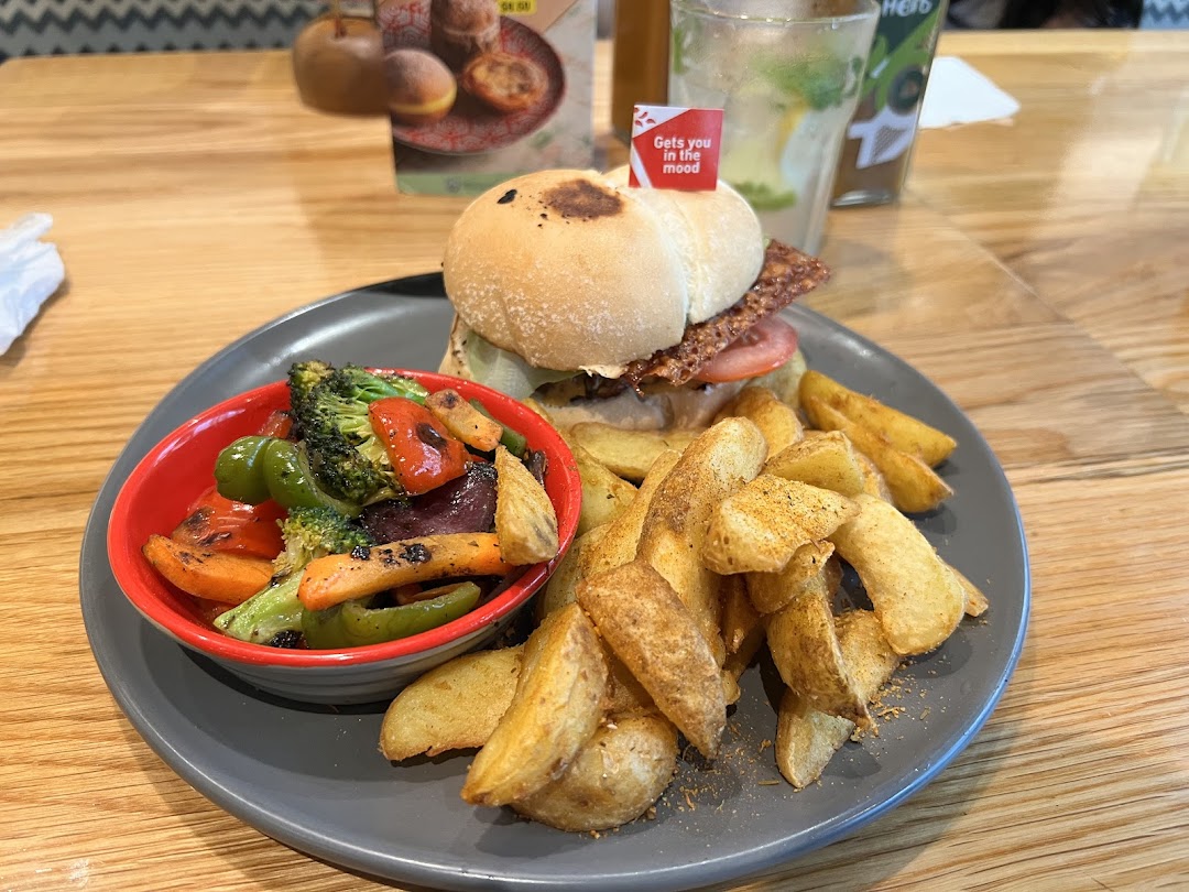 A delicious Nando's meal featuring a chicken burger, PERi-PERi chips, and grilled vegetables on a wooden table.