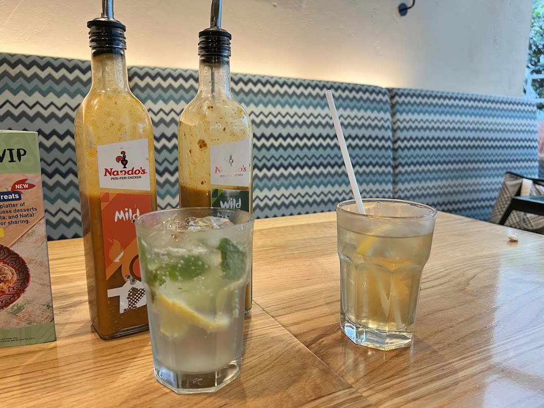 Two Nando's PERi-PERi sauce bottles and refreshing drinks on a wooden table inside the restaurant.