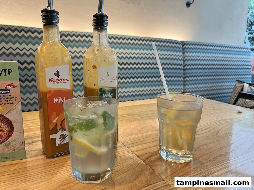 Two Nando's PERi-PERi sauce bottles and refreshing drinks on a wooden table inside the restaurant.
