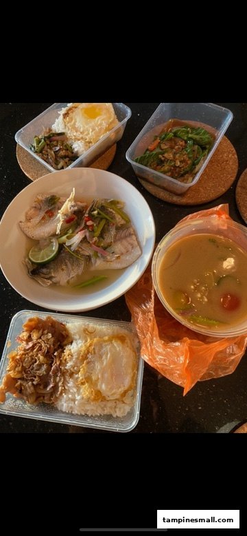 A vibrant spread of authentic Thai dishes, including steamed fish, rice meals with fried eggs, and a soup, some in takeout containers.
