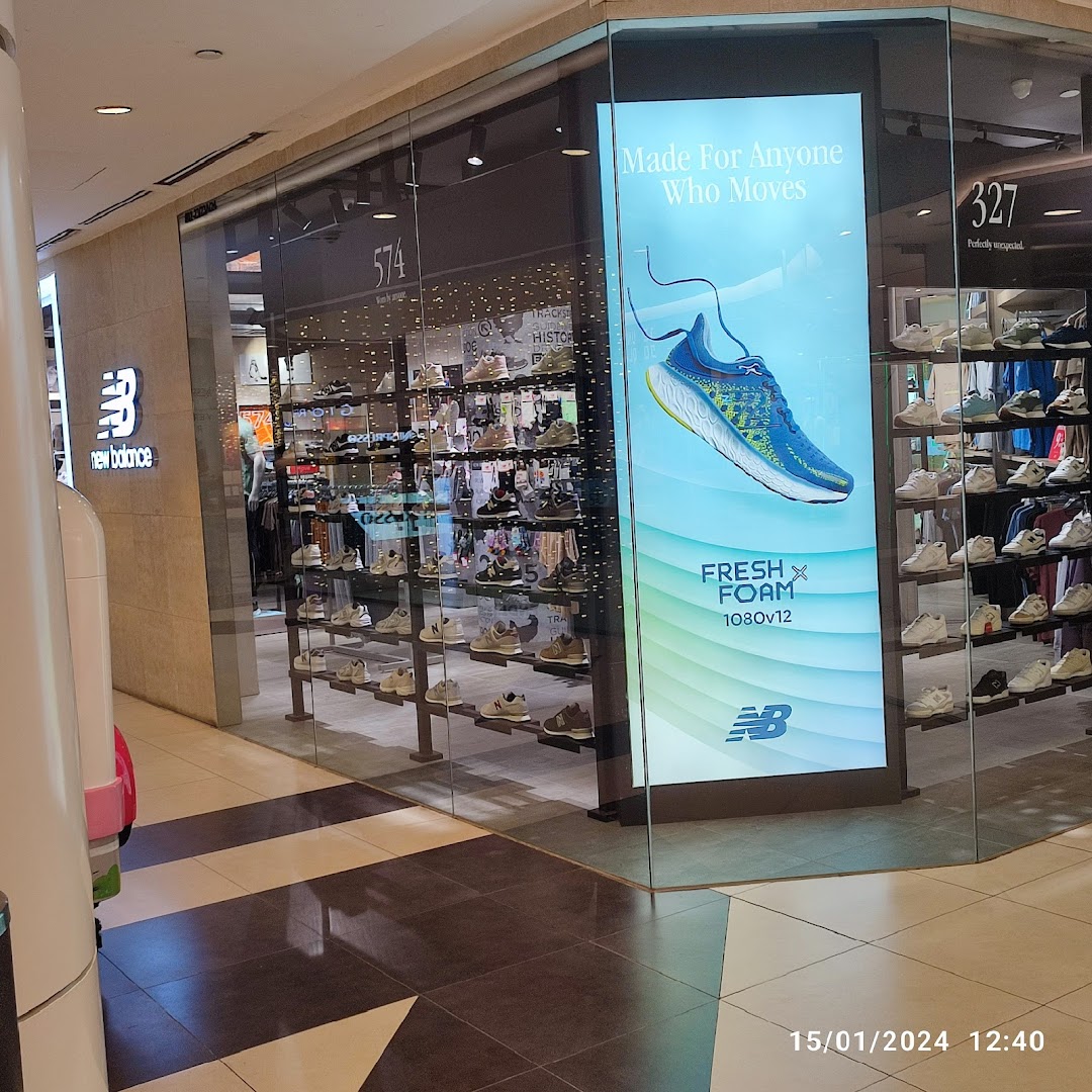 The New Balance shop front features a prominent logo, display windows showcasing numerous shoes, and a large digital advertisement.