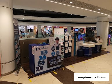 An NTUC LHUB information booth with staff and promotional materials inside Tampines Mall.