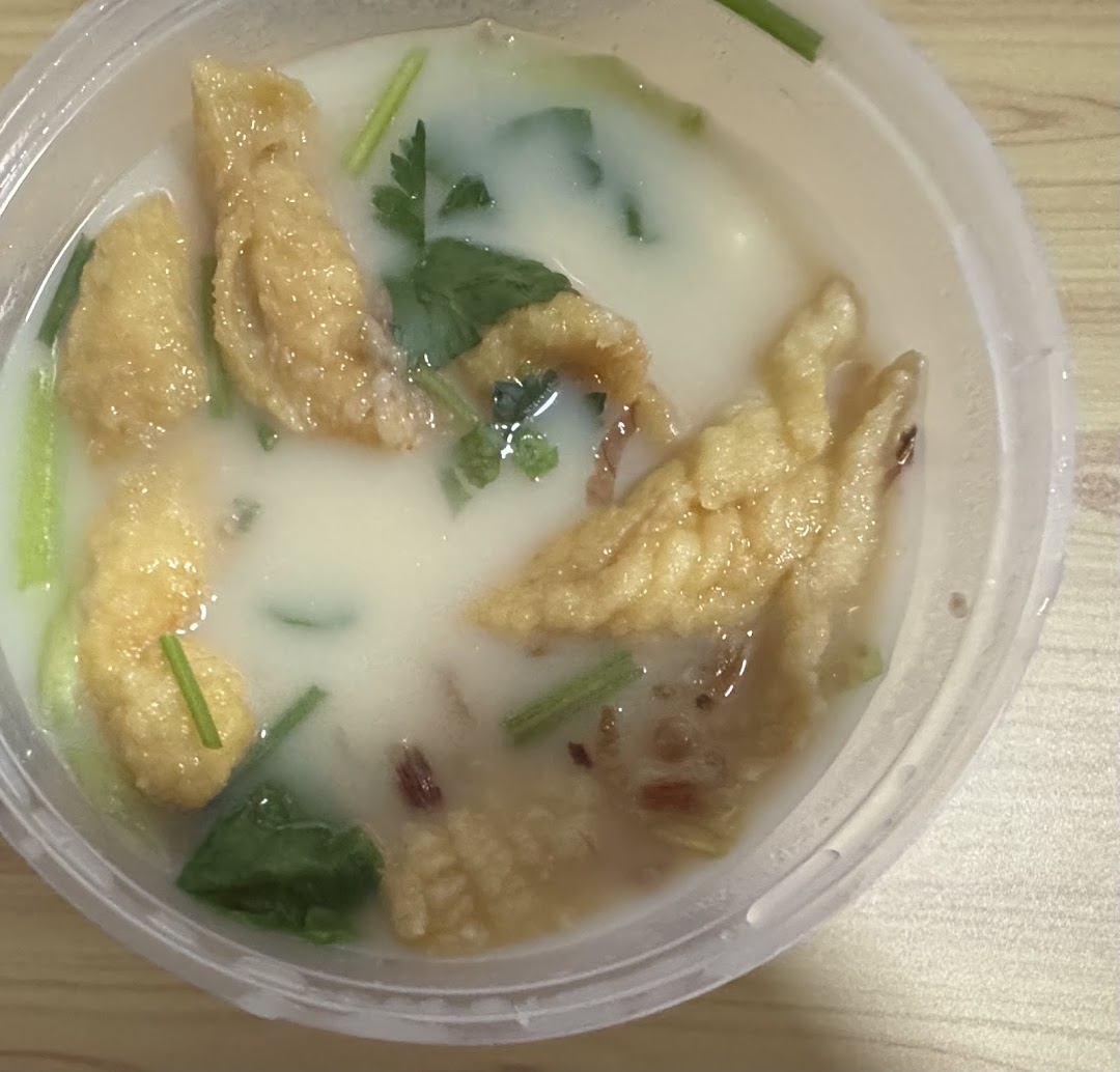 A close-up of a bowl of creamy fish soup with fried fish skin and green garnishes.