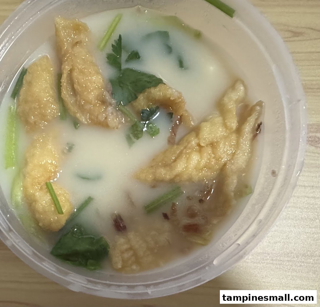 A close-up of a bowl of creamy fish soup with fried fish skin and green garnishes.