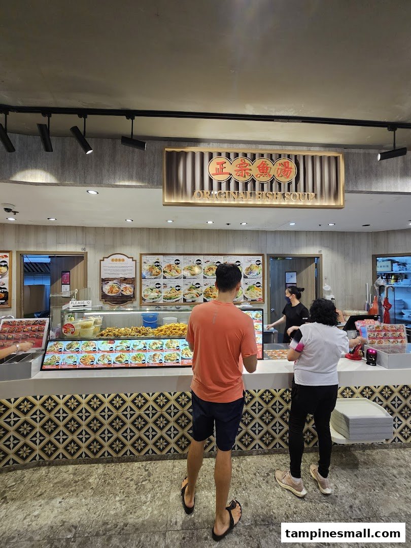Customers order at the counter of Original Fish Soup, showcasing food displays and menu boards.