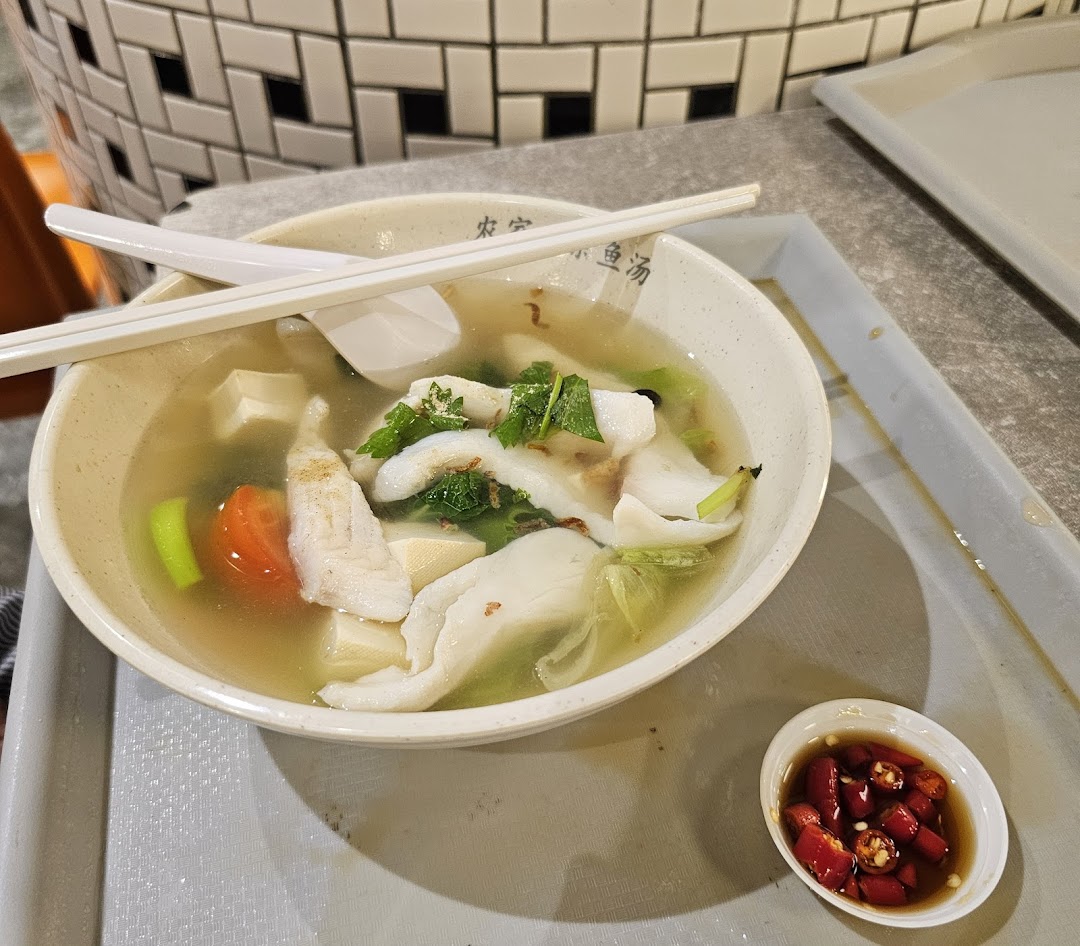 A delicious bowl of fish soup with fresh ingredients, chopsticks, and a side of chili.