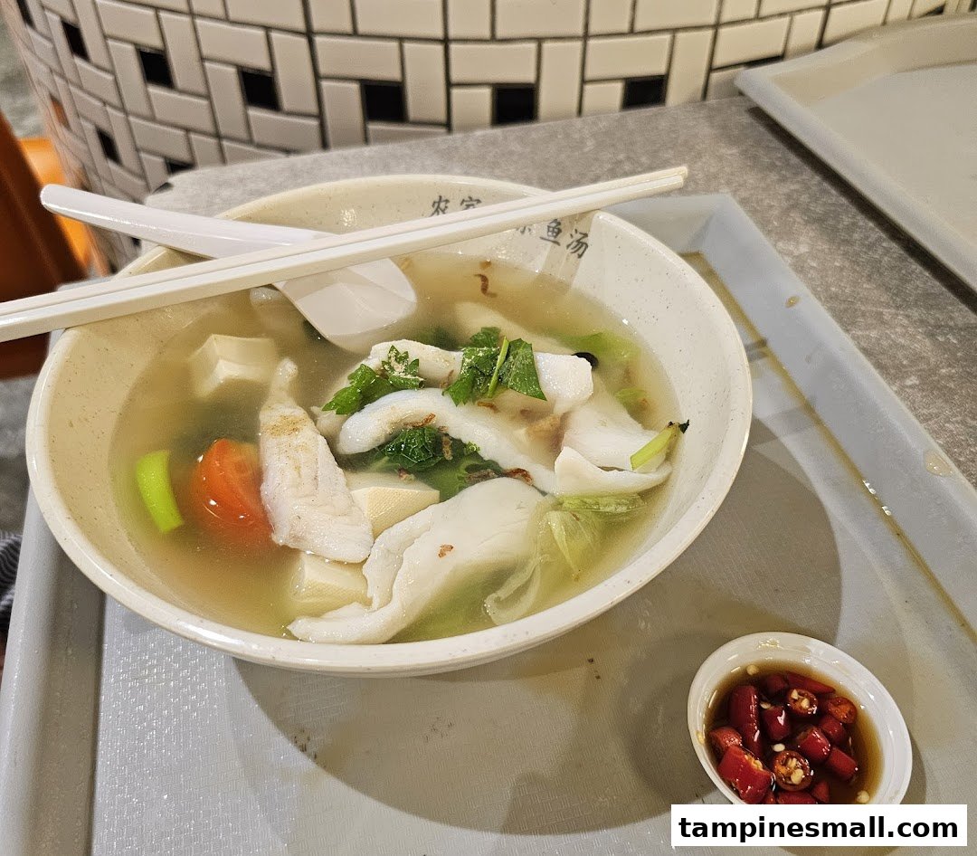 A delicious bowl of fish soup with fresh ingredients, chopsticks, and a side of chili.