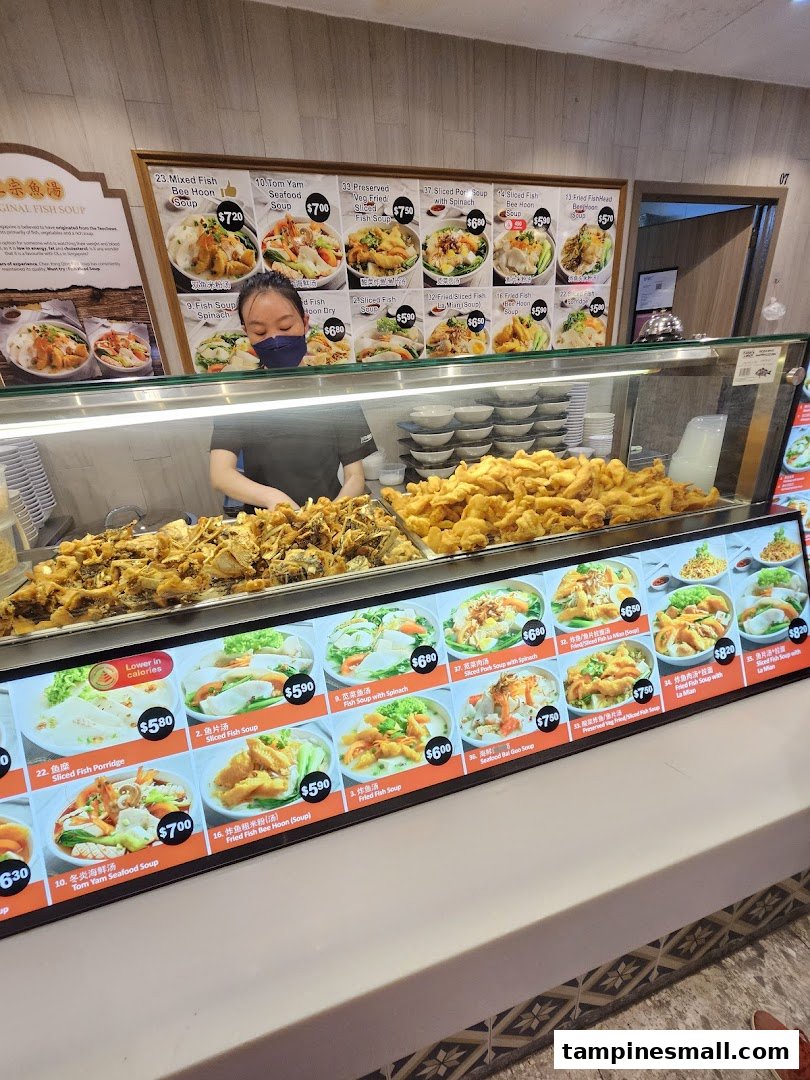 A food stall counter with a staff member, prepared fish dishes, and menu displays.